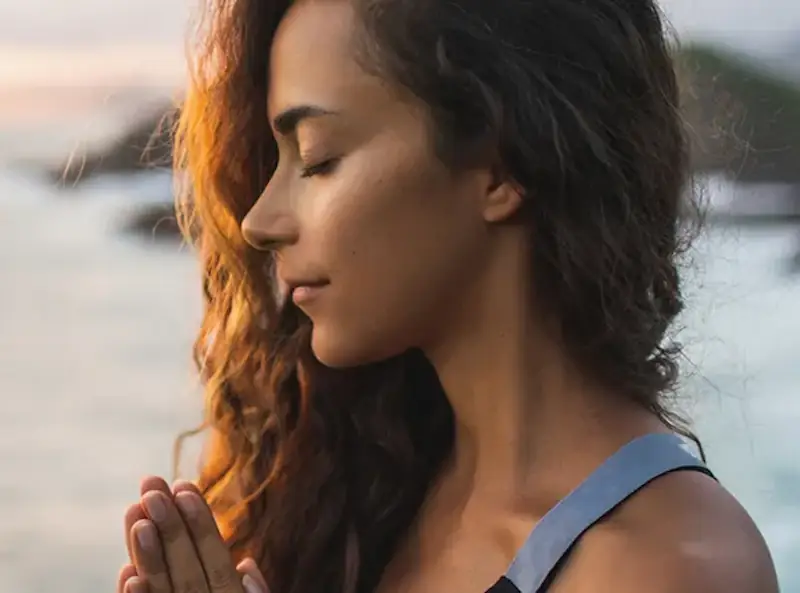 woman with her eyes closed, finding peace within at the ocean shore